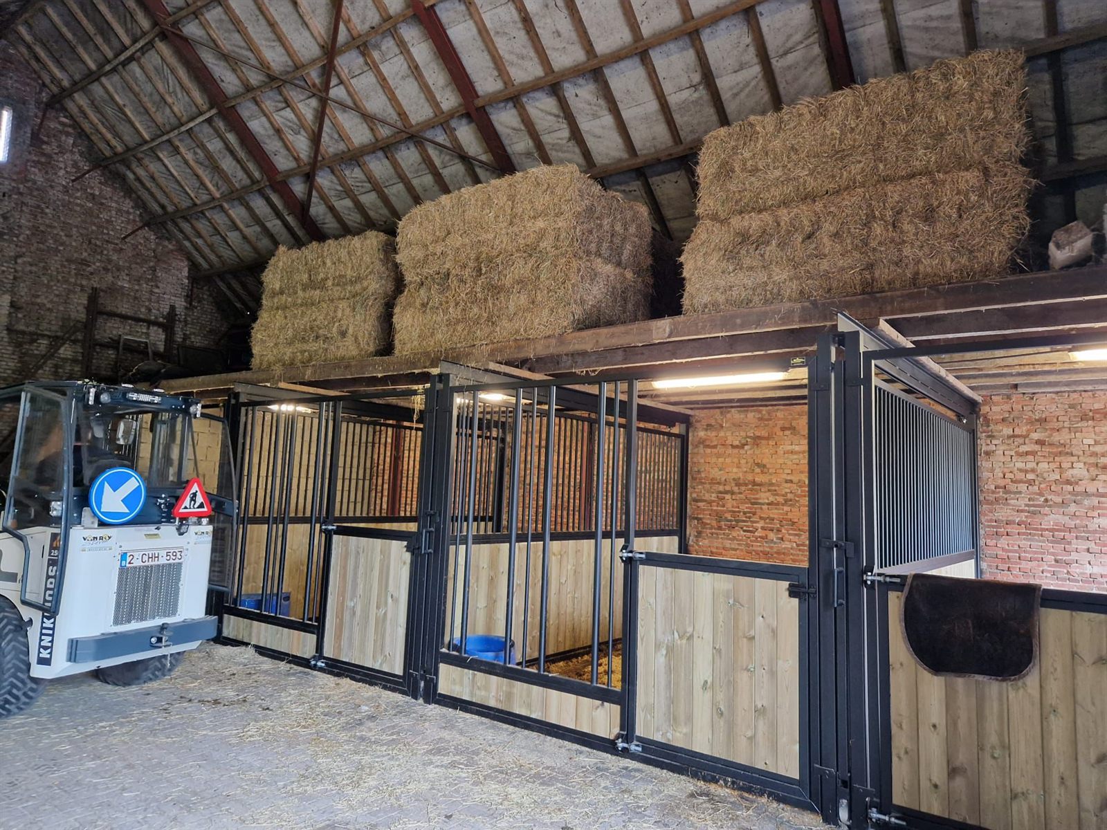 Zwarte paardenboxen met houten panelen in een bestaande stal