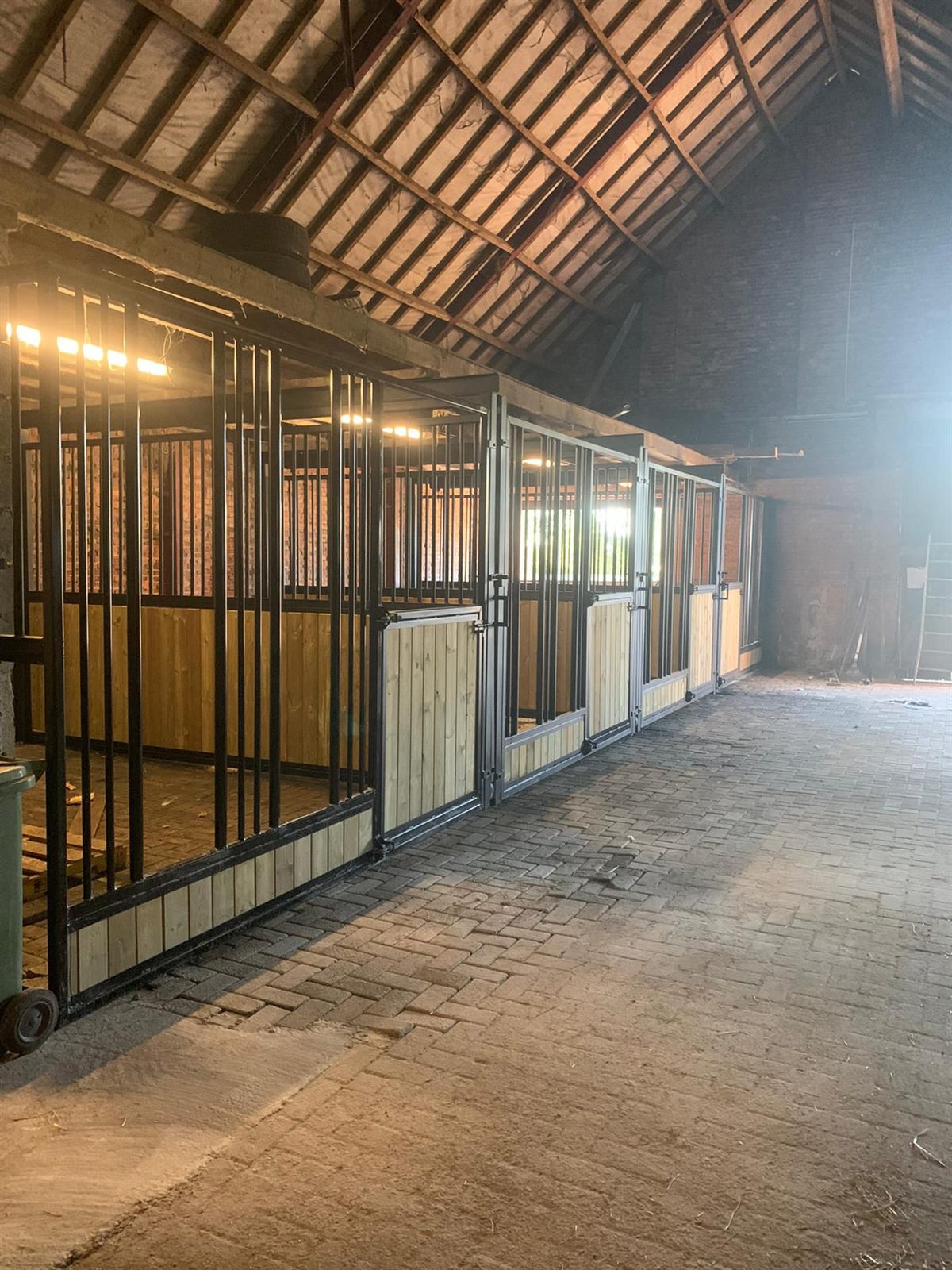 Lange rij afgewerkte paardenboxen met zwarte metalen spijlen en hout